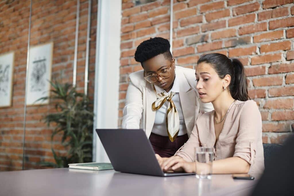 Young businesswoman working on laptop while her CEO is supervising her in the office.